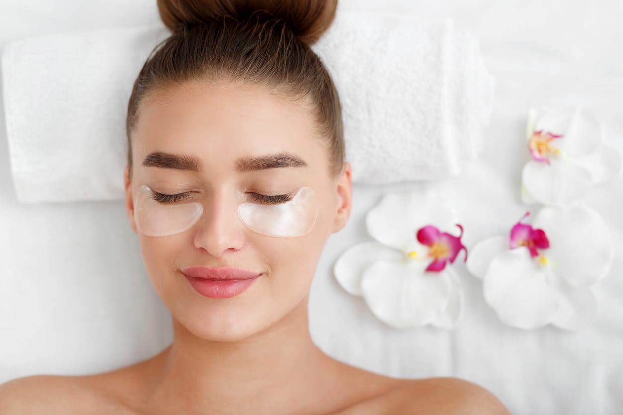 Woman with patches under eyes, relaxing in spa center with flowers nearby