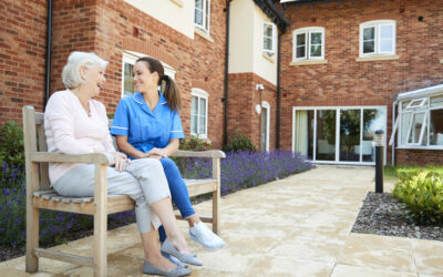 A Senior And Caretaker Sitting On A Bench Just Outside Of A Senior Living Facility